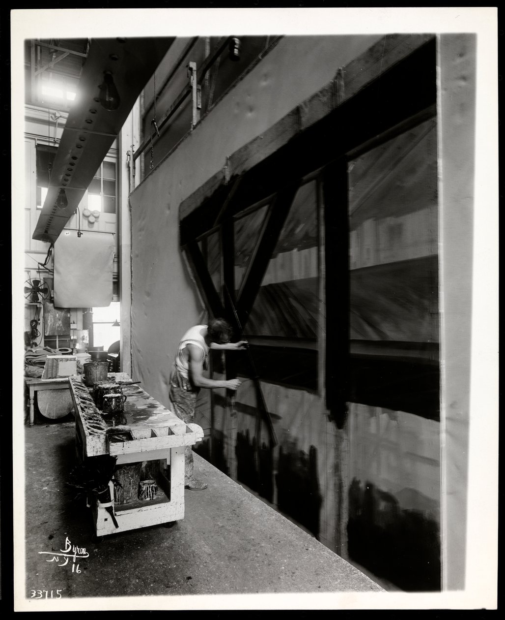 Ein Bühnenmaler malt eine Kulisse in einer Szenenwerkstatt, New York, 1915-6 von Byron Company
