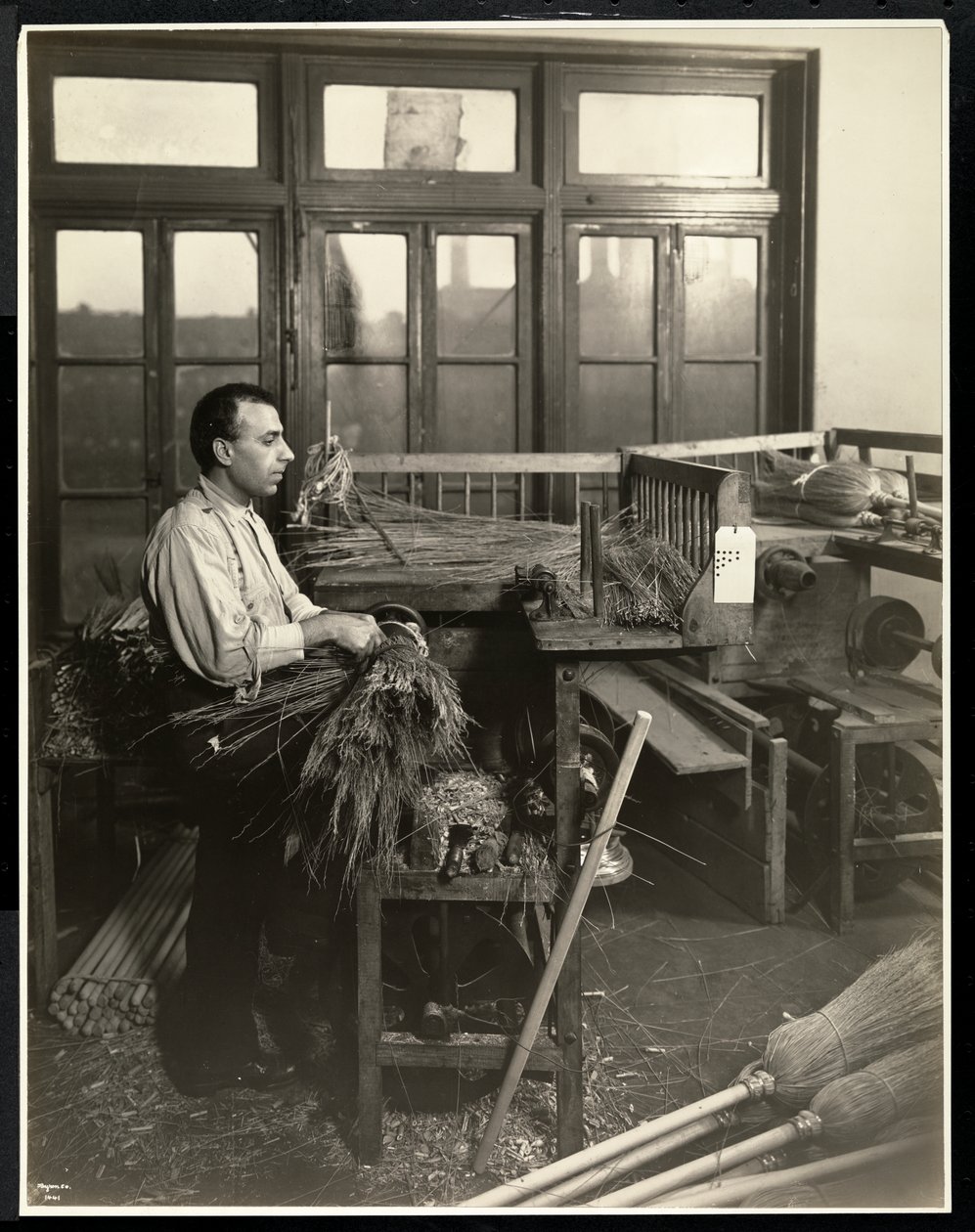 Blinder Mann befestigt Stroh an Besenstielen im Bourne Memorial Building, New York, 1921 von Byron Company