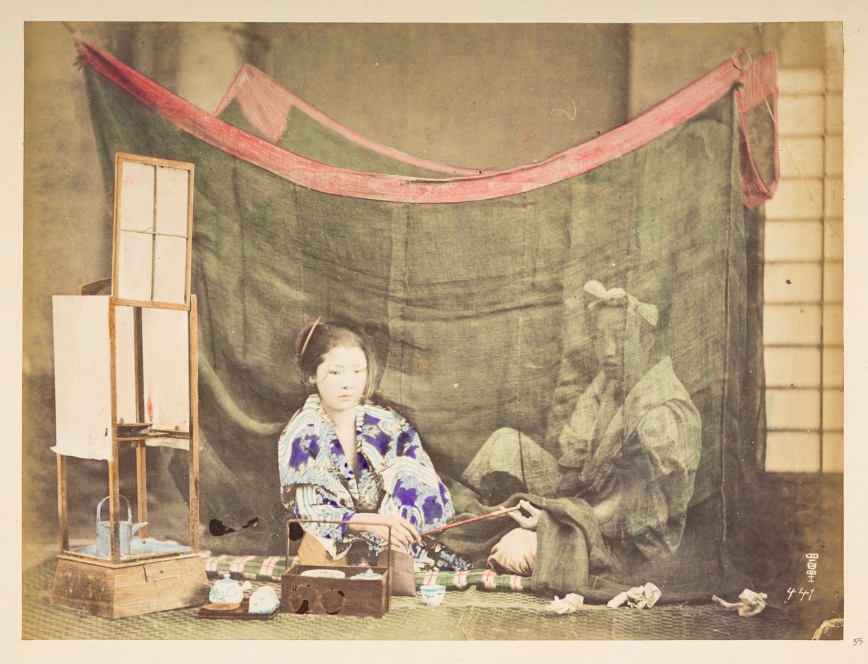 Japanisches Paar in ihrer Freizeit, Studio-Tableau einer jungen japanischen Frau, die mit Teezubehör um sich herum sitzt und eine Pfeife an eine männliche Figur hinter ihr reicht, die von einem Leinen-Moskitonetz abgeschirmt ist, Fotograf: Unbekannt, Lucas von English Photographer