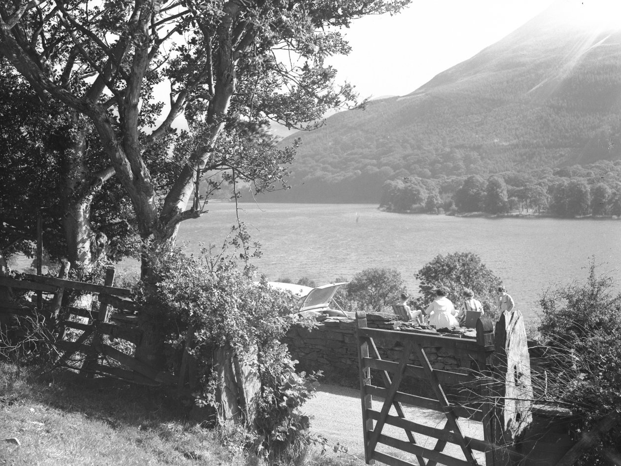 Vier Personen sitzen auf einer Trockenmauer und machen ein Picknick mit Blick auf den See, Auto mit offenem Kofferraum geparkt von Joseph Hardman