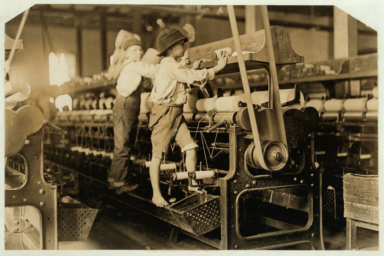 Kleine Jungen klettern auf Spinnrahmen, um gebrochene Fäden zu reparieren und leere Spulen zu ersetzen, Bibb Mill, Macon, Georgia, 1909 von Lewis Wickes Hine