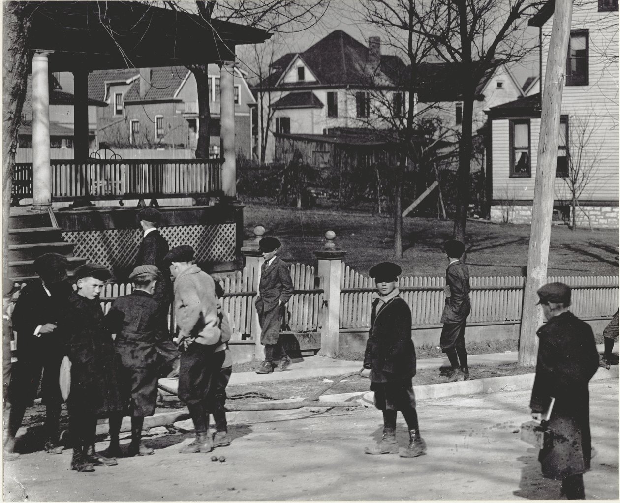 Eine Gruppe von Jungen in Wintermänteln steht auf einer unbekannten Straße entweder vor oder nach einem Schultag. von Unbekannt