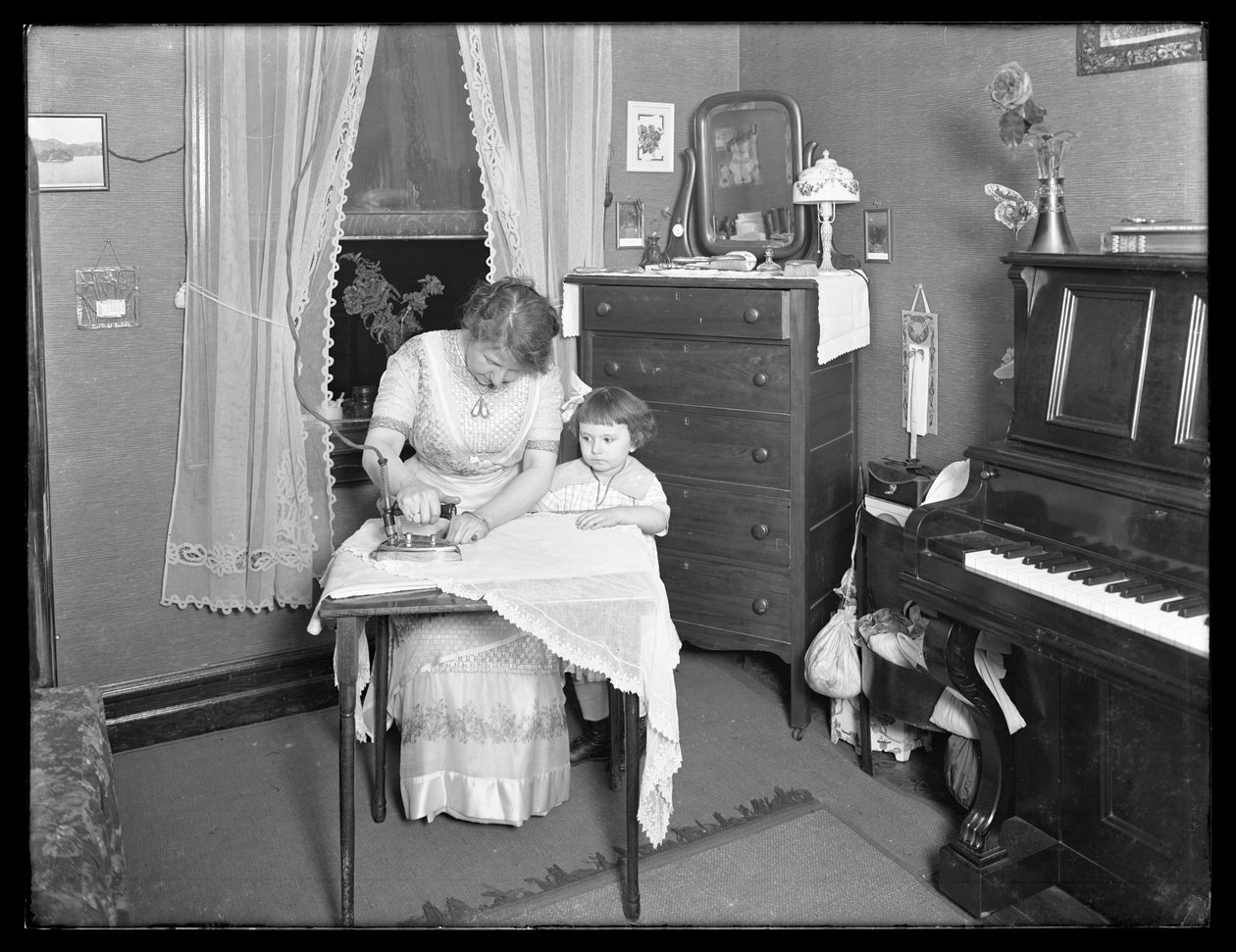 Unidentifizierte Frau demonstriert die Verwendung eines elektrischen Bügeleisens, beobachtet von kleinem Mädchen, ca. 1913-14 von William Davis Hassler