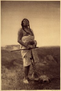 Männlicher Arzt. Wahrscheinlich Sioux, Tintenfisch in der Hand und Büffelschädel zu seinen Füßen.
