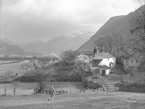 Ein Mann geht auf einen Weg und Gillerthwaite House zu, mit See und Hügeln im Hintergrund