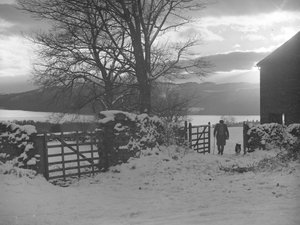 Mann und Hund gehen durch ein Tor zur Kamera im Schnee mit Thirlmere dahinter