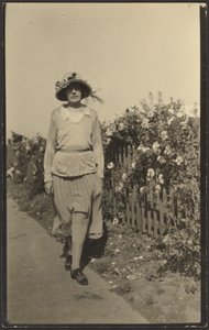 [Frau geht entlang eines Zauns mit Blumen] von Louis Fleckenstein