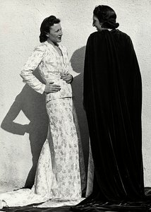 Zwei Modelle präsentieren Kreationen des italienischen Modehauses "Dragoni". Ein Modell trägt ein Outfit aus gemustertem Material, bestehend aus einer Jacke und einem langen Rock mit Schleppe. Das andere Modell, von hinten gesehen, trägt einen langen Samtu