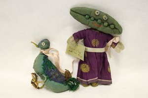 Miss Green Peas Stoffpuppe, Kopf in Form einer Erbsenschote, führt ihre Ente an einem rosa Satinband