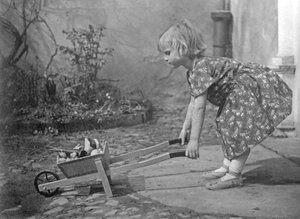 Kleines Mädchen spielt mit einer Schubkarre. Fotografie um 1931 von Unbekannt