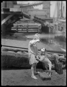 Barfüßiger Junge, möglicherweise William Gray Hassler, spielt mit Hund am Ufer eines Flusses oder Sees, New York, ca. 1910