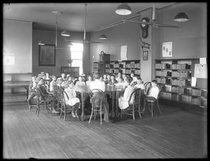 Kinder hören einer Frau im Lesesaal einer nicht identifizierten Filiale der Queens Borough Public Library zu, ca. 1910