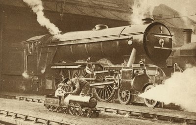 Junge reitet auf einer Spielzeug-Dampflokomotive vor dem echten Ding (s/w Foto) von English Photographer