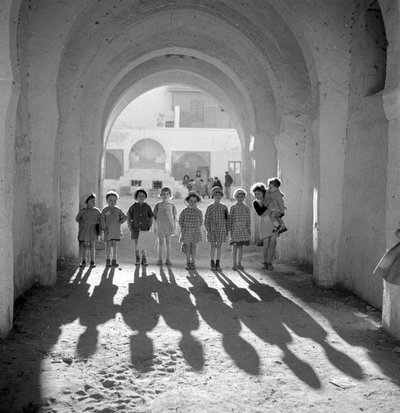 Europäische Kinder in Schuluniform unter einem Bogen mit Schatten. von Maynard Owen Williams