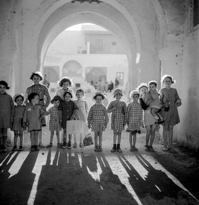 Europäische Kinder in Schuluniform unter einem Bogen mit Schatten. von Maynard Owen Williams