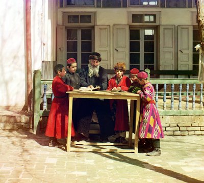 Eine Gruppe jüdischer Kinder mit einem Lehrer auf einem Tisch vor einem Haus, Samarkand, Russisches Reich, zwischen 1905 und 1915 von Sergey Prokudin Gorsky