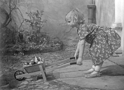 Kleines Mädchen spielt mit einer Schubkarre. Fotografie um 1931 von Unbekannt