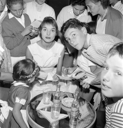 Die Schauspielerin und Model Elsa Martinelli beim XVIII. Internationalen Filmfestival in Venedig Lido (sie gibt jungen Fans Autogramme. Auf dem Tisch eine Flasche Schweppes) - 1957 von Unbekannt