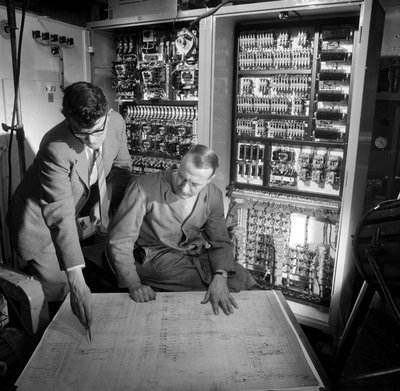 Ingenieure diskutieren Pläne vor dem elektronischen Bedienfeld, das sie gebaut haben von Frederick (attr. to) Barnard