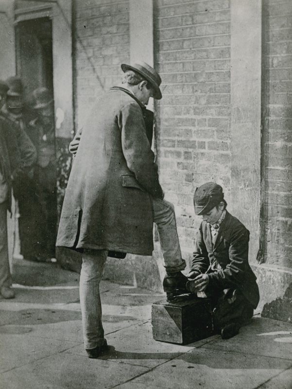 Ein junger Schuhputzer putzt die Schuhe eines Mannes auf der Straße von English Photographer