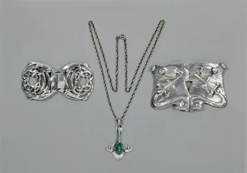 Silberschmuck entworfen für Liberty. Von links nach rechts: Taillenspange mit verschlungenem keltischem Design, 1904. Anhänger und Kette mit Cabochon-Schliff Chrysopras. Taillenspange mit Repousse-Design auf gehämmertem