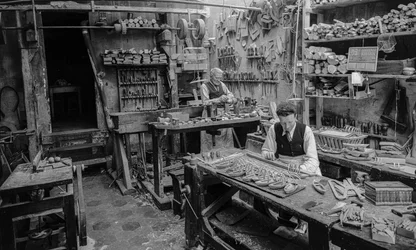 Handwerker an einer Werkbank in einer Werkstatt, die kleine Holzobjekte herstellen, die weder...