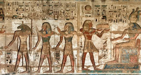 Ägyptische Antiquität: erster Hof, Detail der bemalten Reliefs, die den Pharao darstellen, der den Göttern Horus und Khnoum Opfergaben bringt. Totentempel von Ramses III (1187-1156 v. Chr.). Luxor, Medinet Habou, Ägypten