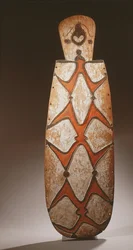 Ovaler Asmat-Schild, geschnitzt mit stilisierten Figuren, eine Maske oben