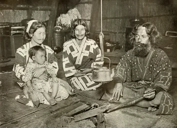 Ainu-Mann und -Frauen zu Hause, 1910