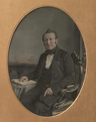 Sitzender Mann zeigt auf eine Passage in einem offenen Buch, 1850er