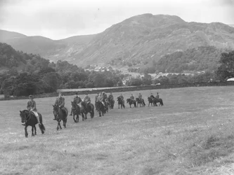 Eine Gruppe von Männern, die in einer Reihe auf Ponys wandern, mit Hügeln im Hintergrund