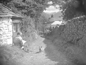 Eine Frau sitzt lesend mit einem Hund in einer Gasse