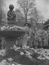Kinder legen Narzissensträuße auf einen Brunnen mit Statue oben