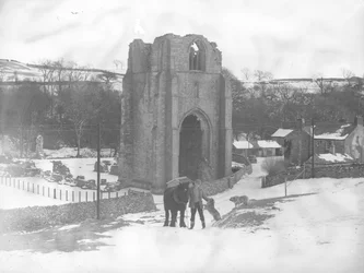 Mann mit Pferd und zwei Hunden vor den Überresten der Shap Abbey im Schnee