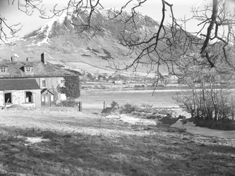 Das Anglers Hotel in Ennerdale mit Bäumen im Vordergrund und gefrorenem See und verschneiten Hügeln dahinter