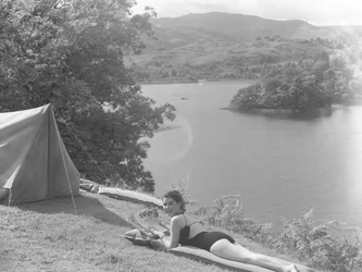 Ansicht einer jungen Frau im Badeanzug, die auf einer Luftmatratze liegt, See im Hintergrund