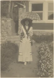 [Frau im Vorgarten mit Kamera und kariertem Regenschirm]