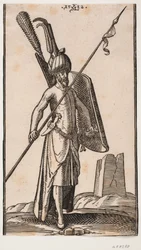Stehender Soldat mit krummem Schild in der linken Hand und einem schräg gehaltenen Speer in der rechten Hand; Schwert an seiner linken Seite, ein Dolch im Gürtel an seiner linken Seite; im Hintergrund rechts die Ruine eines Obelisken oder eines Turms mit q