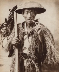 Japanischer Kuli (Landarbeiter) mit einem Hut, um sich vor starkem Regen in den Reisfeldern zu schützen (s/w Foto)