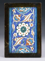 Eine Iznik-Randfliese mit einer zentralen Blütenknospe zwischen rollenden Palmetten und blättriger Ranke, ca. 1570