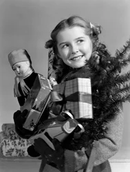 Junges Mädchen trägt einen Arm voller Weihnachtsgeschenke, ca. 1950