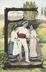 E: Ein Mann in Weiß und Rot steht zwischen zwei Frauen, die Rock, Mieder und Schürze tragen. Ländliche Umgebung - Alphabet Figuren Ref Th. E., L. Theochrom - Serie 994. Theodor Eisman, Verleger, Leipzig