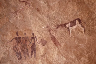 Felskunst, Vorgeschichte: Felsmalerei einer Gruppe von Figuren und einer zweifarbigen Kuh mit großen Hörnern in einem verzierten Schutzraum im Uweinat-Massiv, Ägypten. (Zeitraum von 8000 bis 3000 v. Chr.). Fotografie