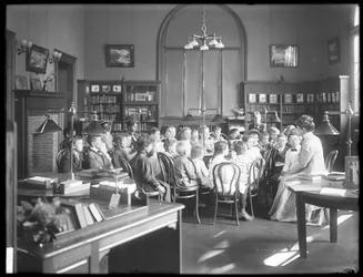 Kinder hören einer Frau im Lesesaal einer nicht identifizierten Filiale der Queens Borough Public Library zu, ca. 1910