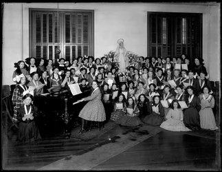 Gruppenporträt einer Mädchenchor-Klasse, die sich um ein Klavier versammelt und Noten hält, wahrscheinlich im römisch-katholischen Waisenhaus in Kingsbridge, Bronx, ca. 1911