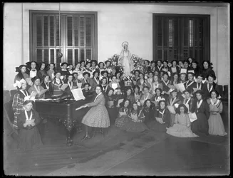 Gruppenporträt einer Mädchenchor-Klasse, die sich um ein Klavier versammelt und Notenblätter hält, wahrscheinlich im römisch-katholischen Waisenhaus in Kingsbridge, Bronx, um 1911