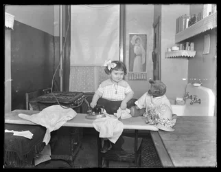 Unidentifiziertes kleines Mädchen, das die Verwendung eines elektrischen Bügeleisens demonstriert, c.1913-14